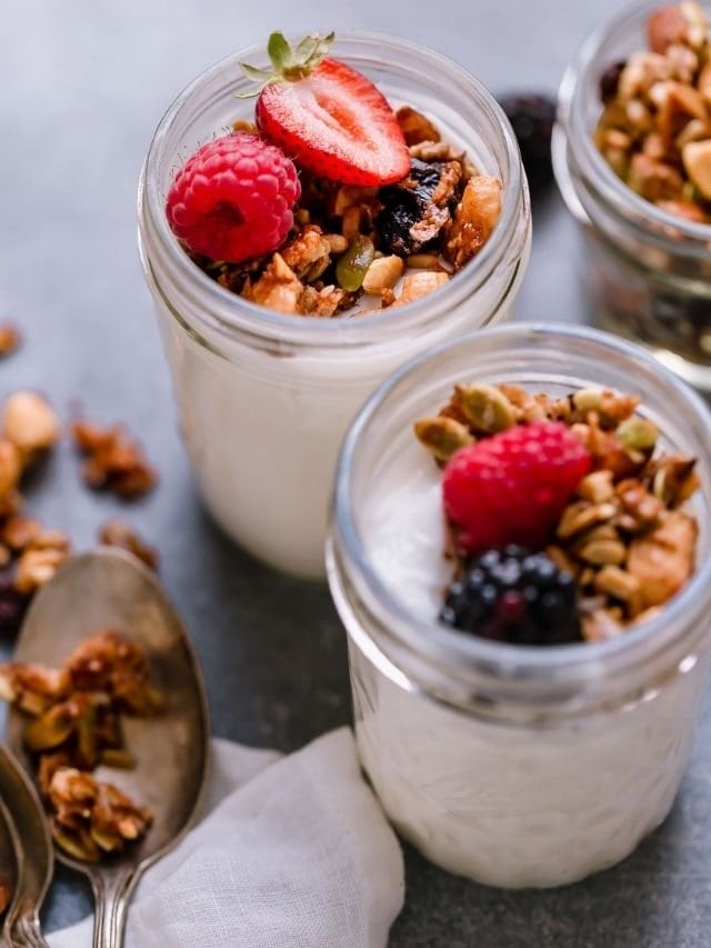 Paleo granola with honey and cinnamon topping small mason jars filled with yogurt, fresh berries on top.